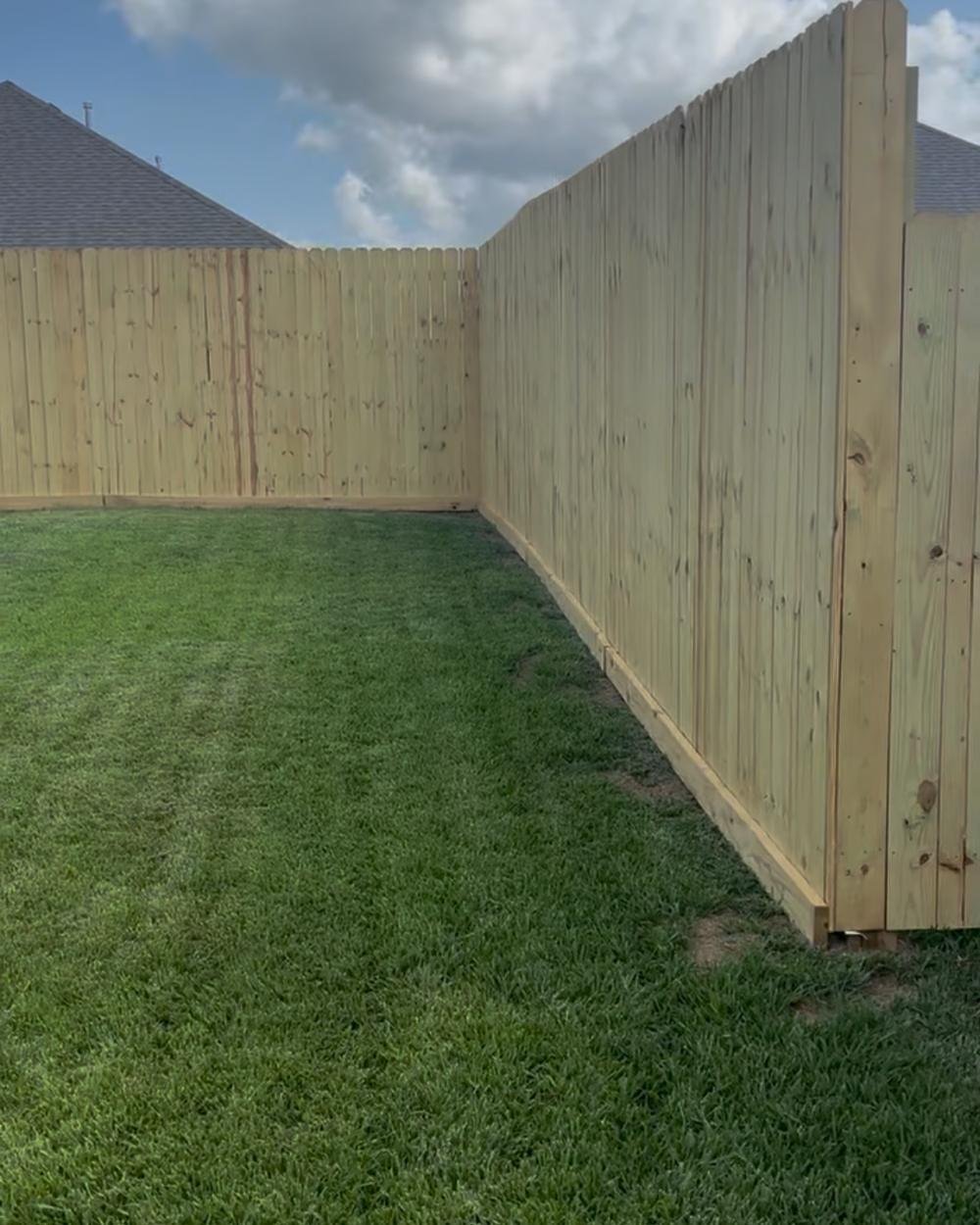 A new pine privacy fence running straight along a green backyard