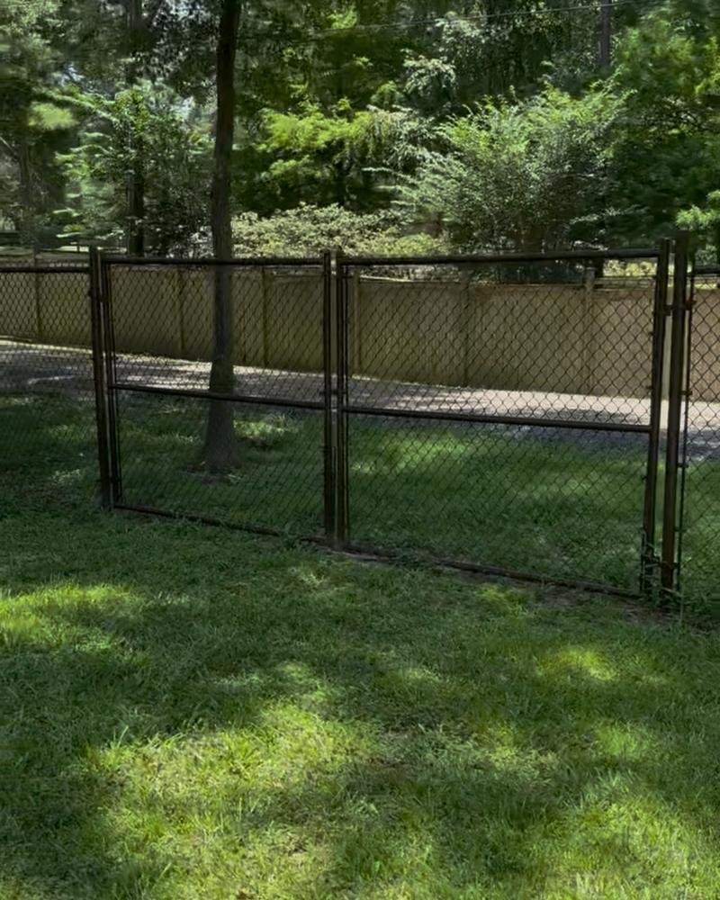 Black chain-link fence with a double drive gate in a shaded yard